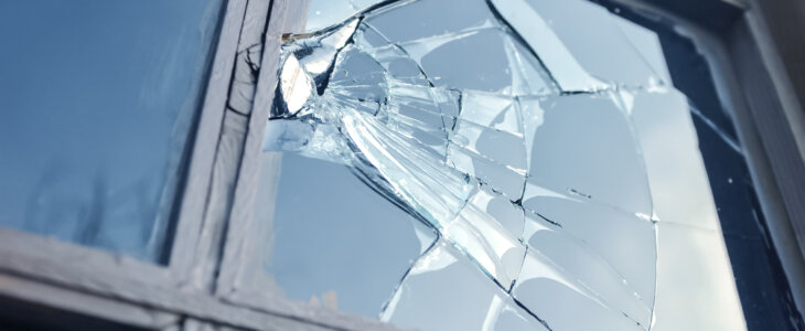 Broken glass window reflecting blue sky.