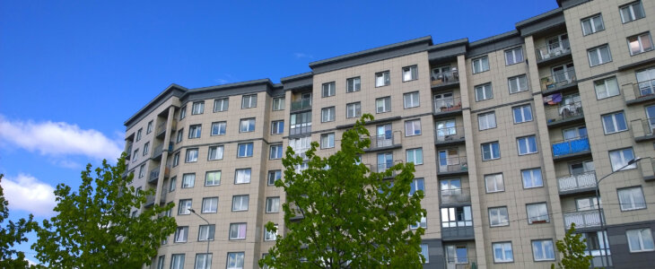 Facade of a new multi-story residential building. Sale and rental of economy class apartments and comfortable housing for young families. Cityscape. City living. Real estate. Blue sky. Green tree.