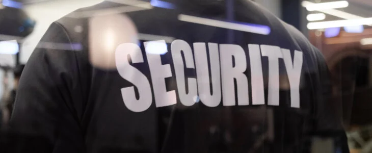 A security guard standing inside a commercial building nearby the window reflecting light.