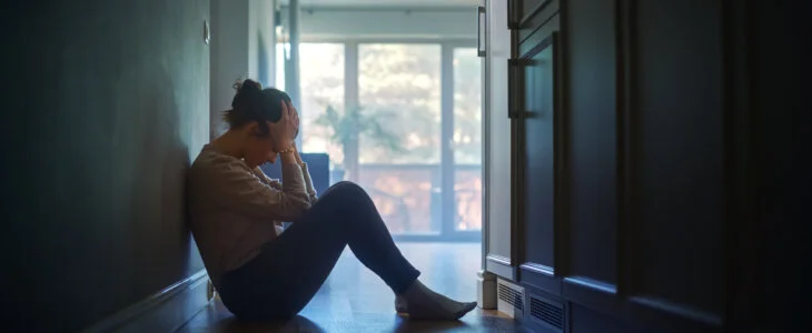 Sad Young Woman Sitting on the Floor In the Hallway of Her Appartment, Covering Face with Hands. Atmosphere of Depression, Trouble in Relationship, Death in the Family. Dramatic Bad News Moment